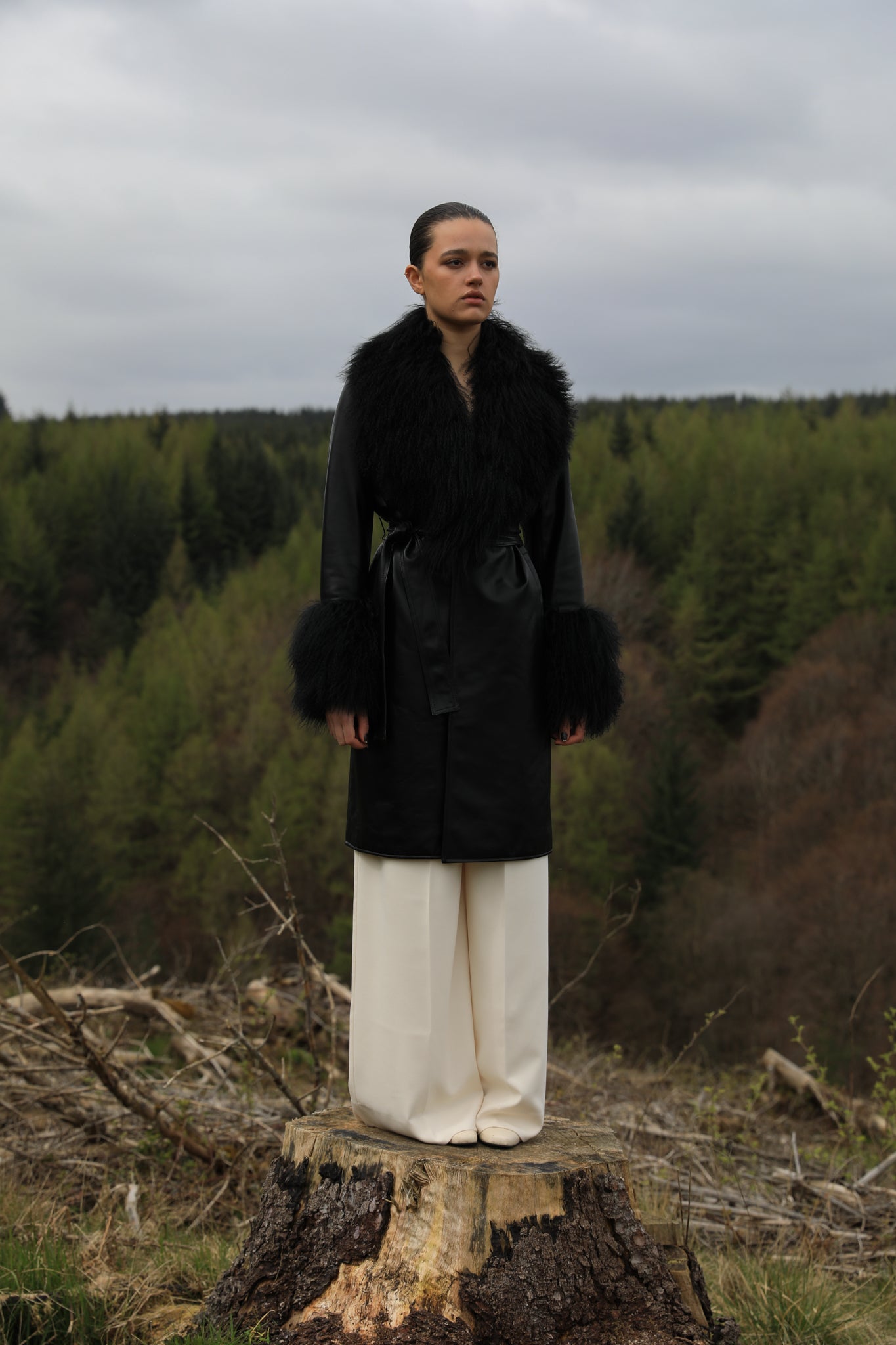 Black genuine leather trench wrap coat with Mongolian collar and cuffs, designed by Josephine Jones. This elegant outerwear piece exudes sophistication and warmth, perfect for elevating any ensemble with its luxurious texture and timeless style.