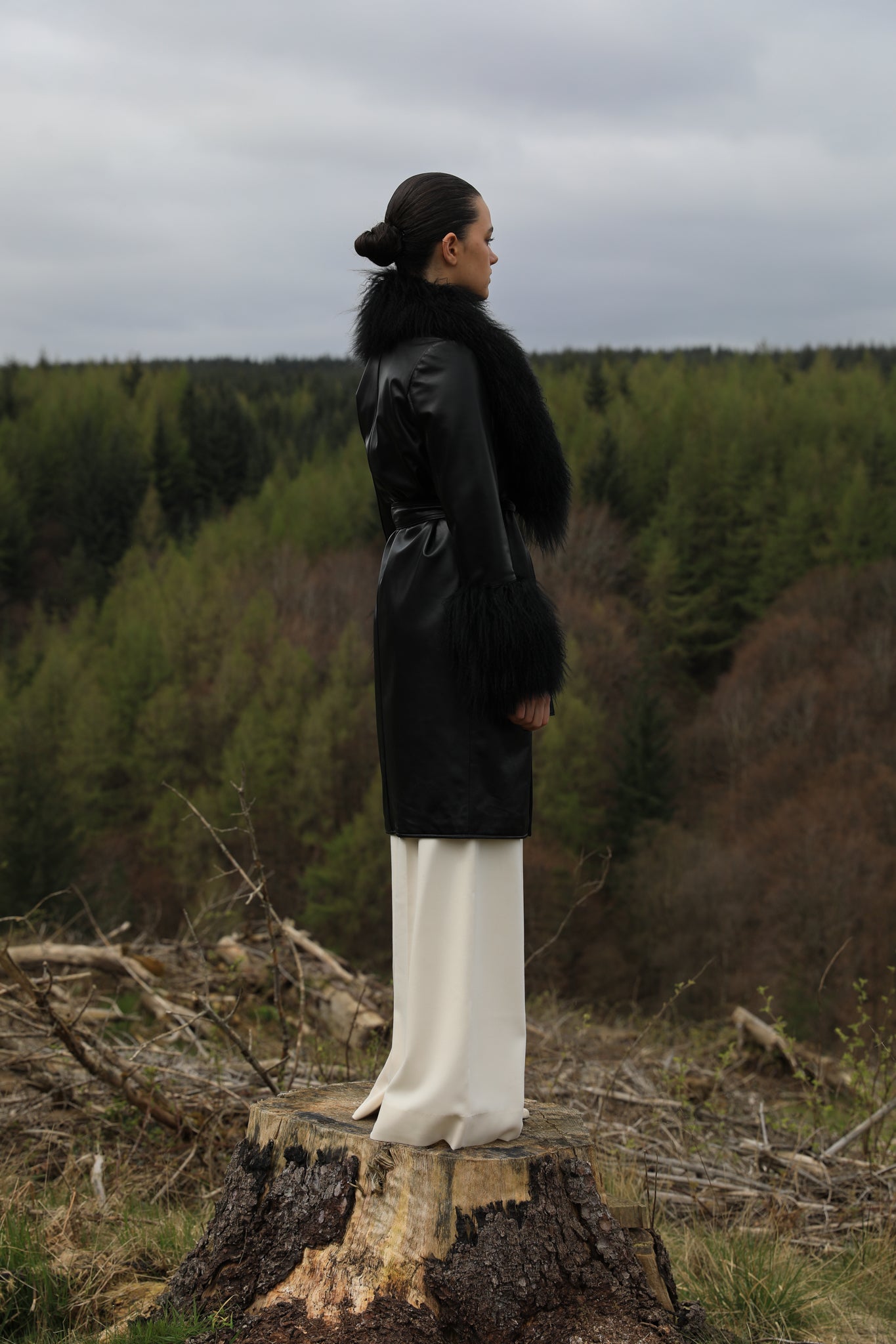 Black genuine leather trench wrap coat with Mongolian collar and cuffs, designed by Josephine Jones. This elegant outerwear piece exudes sophistication and warmth, perfect for elevating any ensemble with its luxurious texture and timeless style.