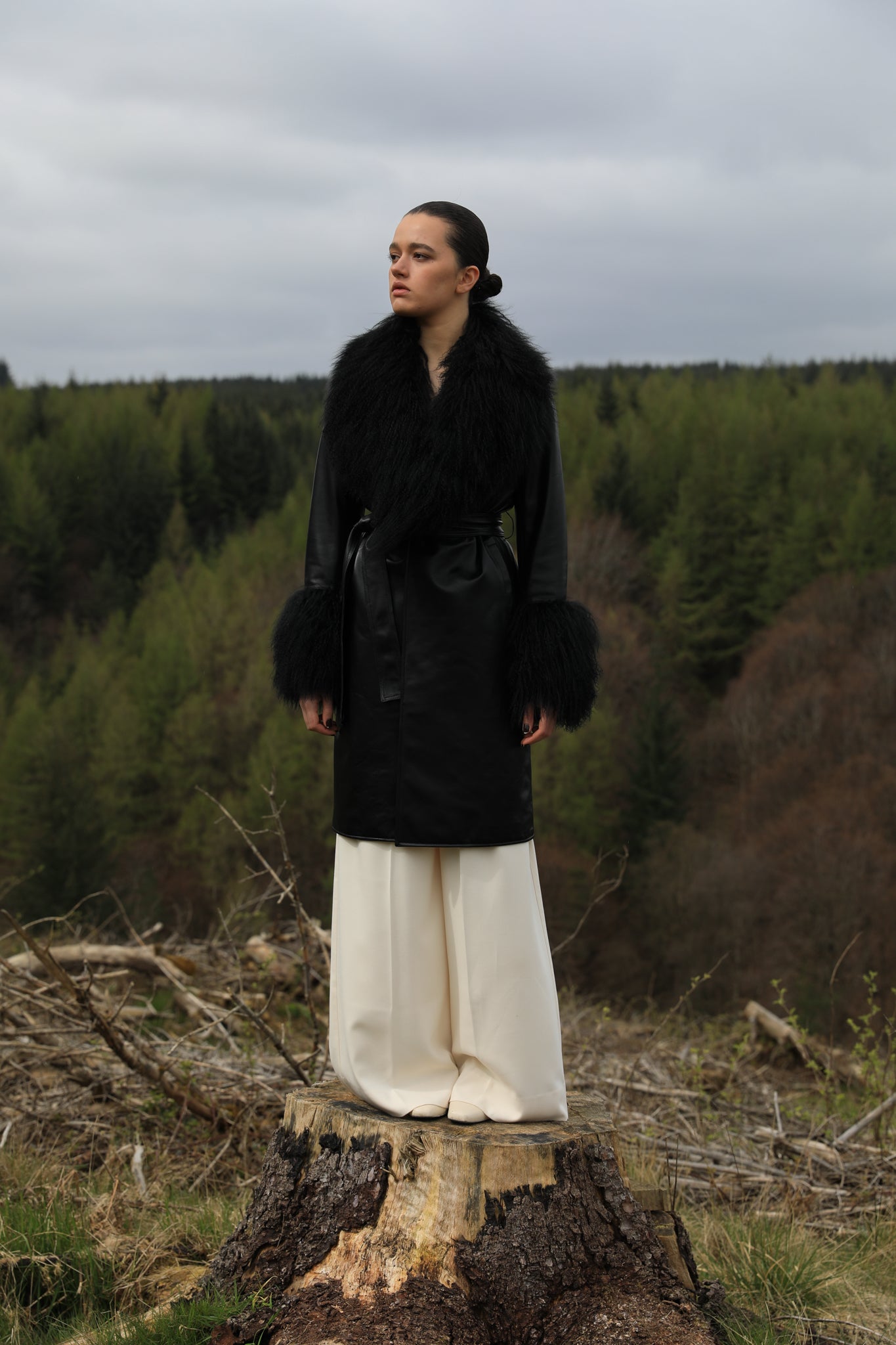 Black genuine leather trench wrap coat with Mongolian collar and cuffs, designed by Josephine Jones. This elegant outerwear piece exudes sophistication and warmth, perfect for elevating any ensemble with its luxurious texture and timeless style.