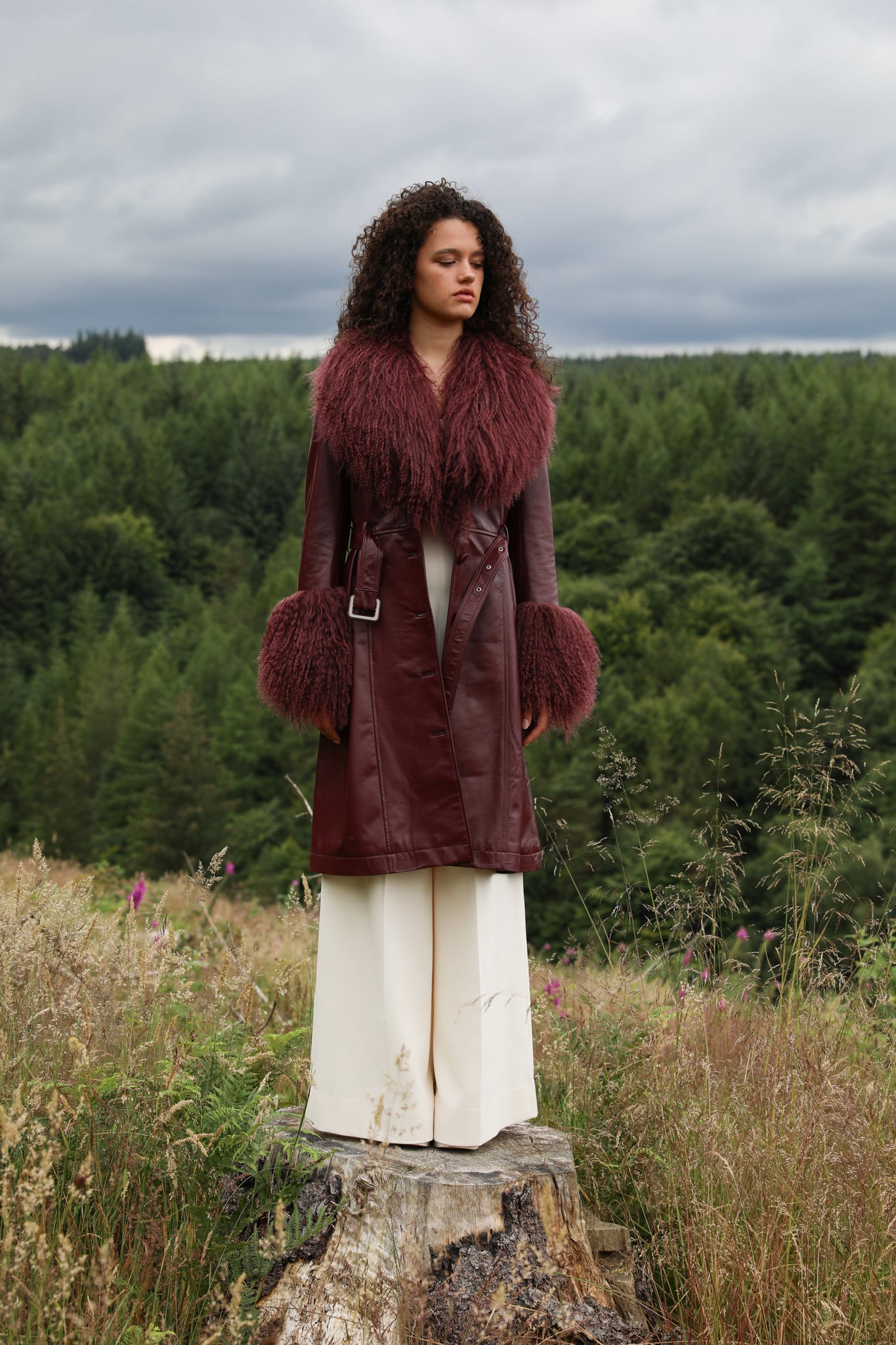 A sophisticated burgundy trench coat with a plush Mongolian collar and cuffs, crafted from genuine leather by Josephine Jones. Elevate your style with this luxurious outerwear piece.