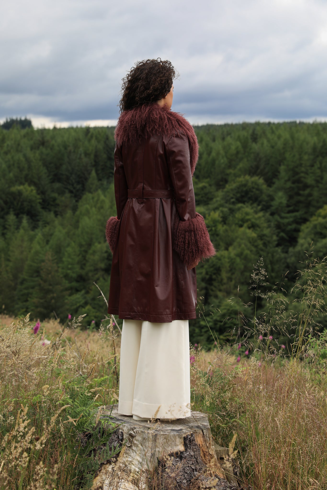 A sophisticated burgundy trench coat with a plush Mongolian collar and cuffs, crafted from genuine leather by Josephine Jones. Elevate your style with this luxurious outerwear piece.