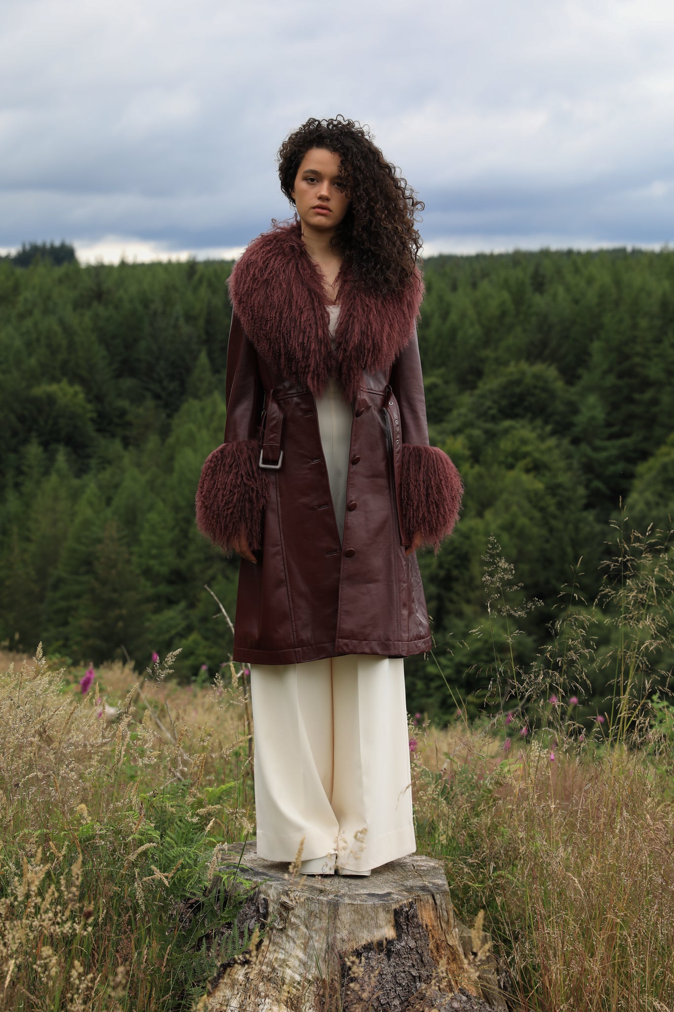 A sophisticated burgundy trench coat with a plush Mongolian collar and cuffs, crafted from genuine leather by Josephine Jones. Elevate your style with this luxurious outerwear piece.