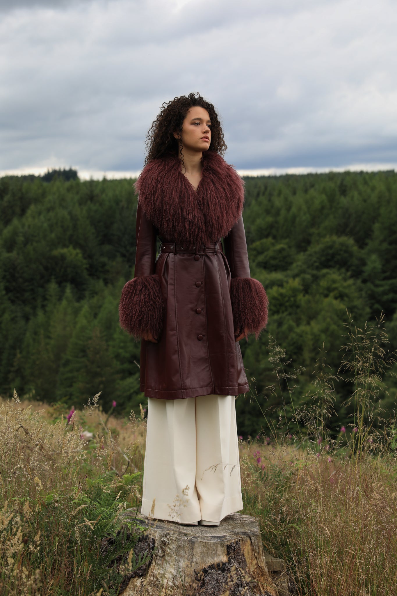 A sophisticated burgundy trench coat with a plush Mongolian collar and cuffs, crafted from genuine leather by Josephine Jones. Elevate your style with this luxurious outerwear piece.