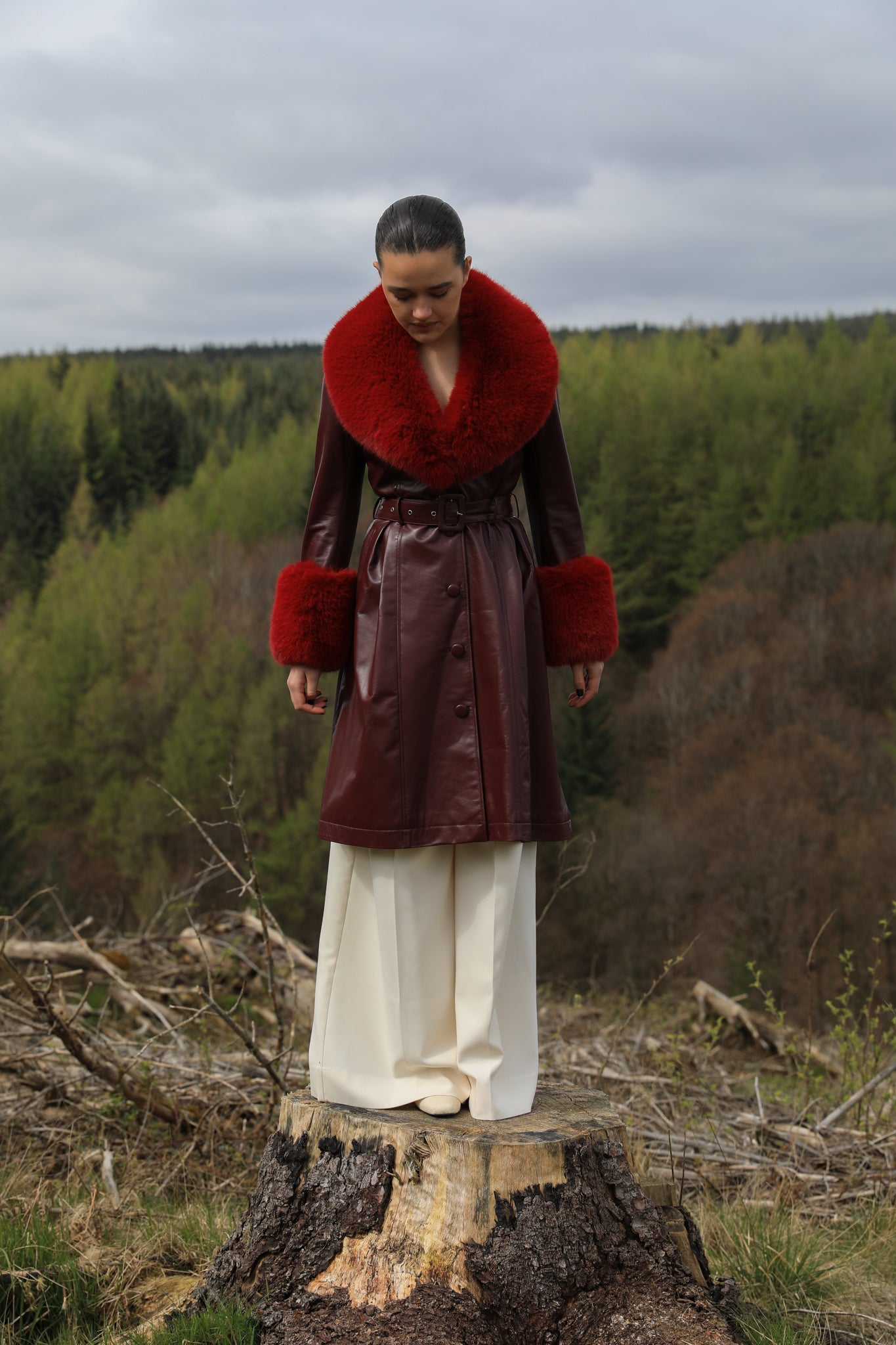 A sophisticated burgundy trench coat with Bordeaux faux fur collar and cuffs, crafted from genuine leather by Josephine Jones. This luxurious outerwear piece exudes elegance and warmth, perfect for chic winter styling.