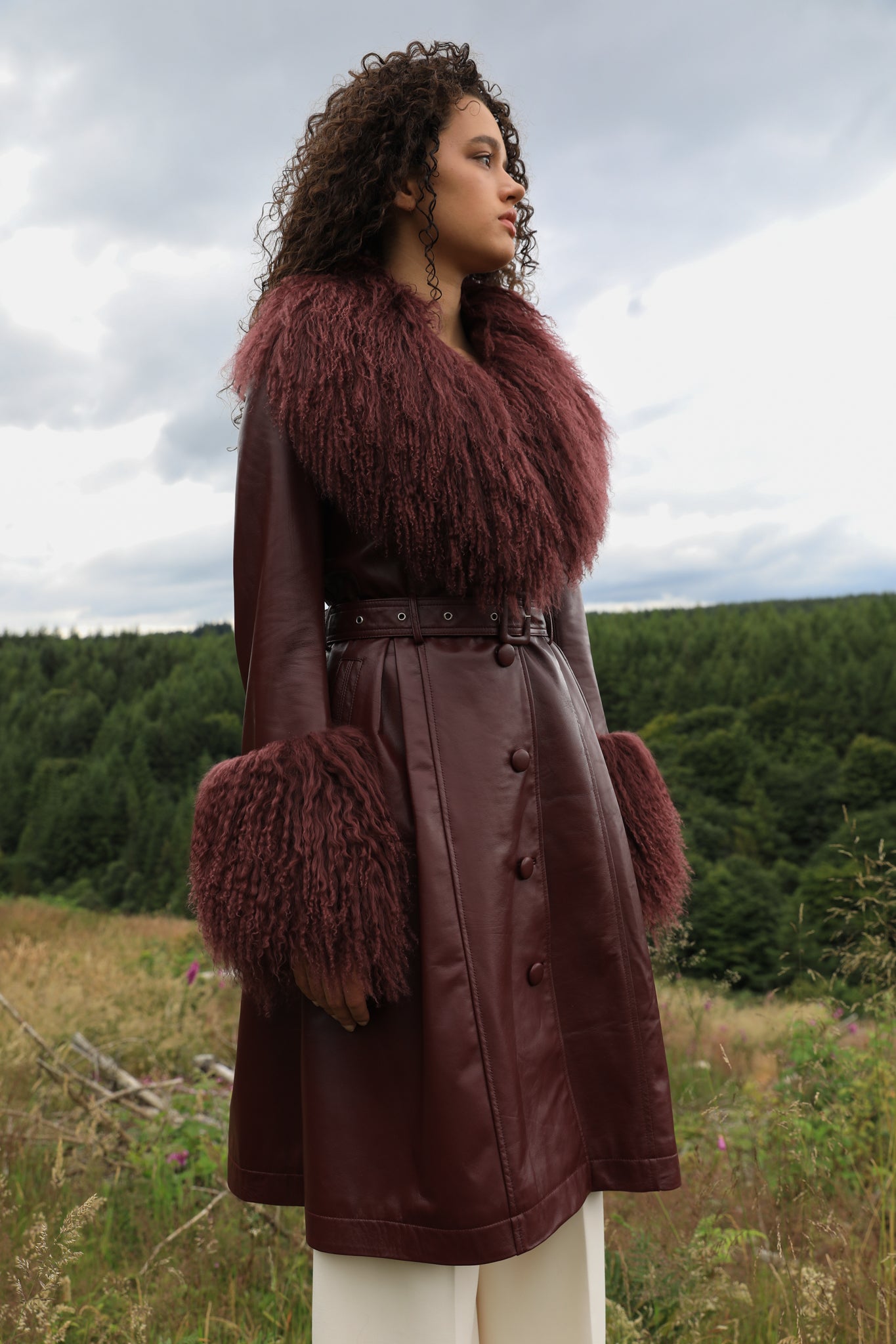 A sophisticated burgundy trench coat with a plush Mongolian collar and cuffs, crafted from genuine leather by Josephine Jones. Elevate your style with this luxurious outerwear piece.