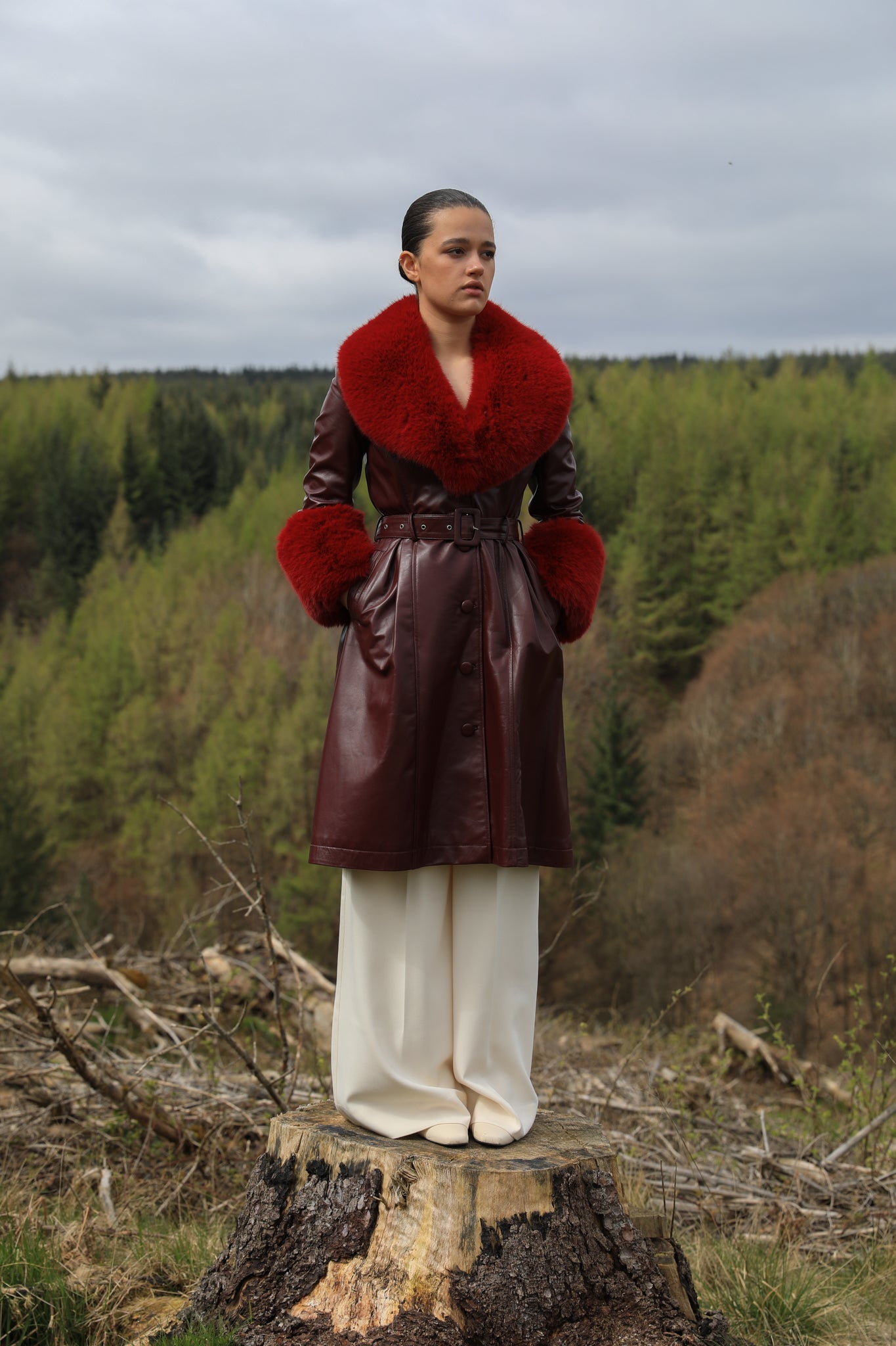 A sophisticated burgundy trench coat with Bordeaux faux fur collar and cuffs, crafted from genuine leather by Josephine Jones. This luxurious outerwear piece exudes elegance and warmth, perfect for chic winter styling.