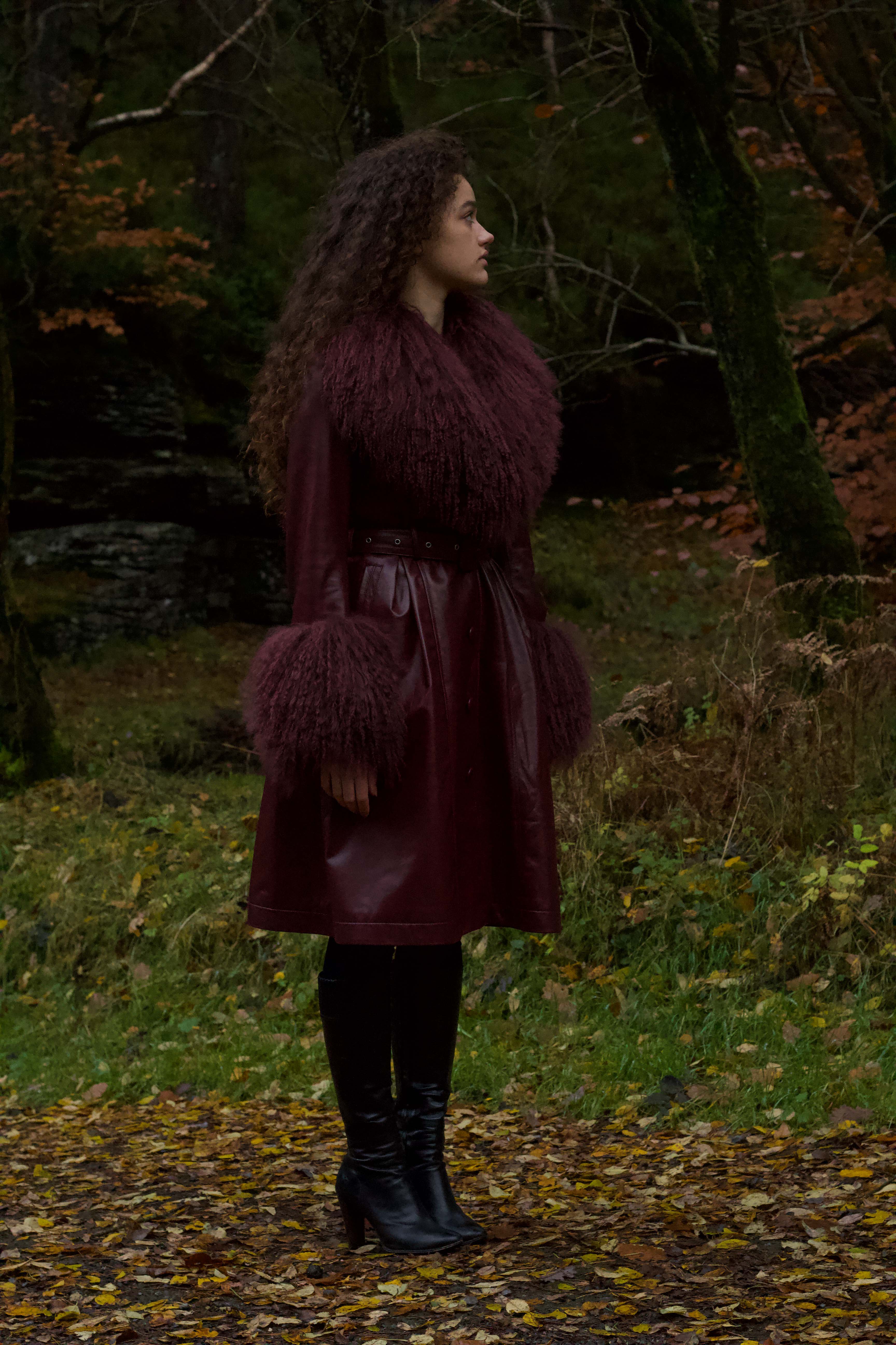 A sophisticated burgundy trench coat with a plush Mongolian collar and cuffs, crafted from genuine leather by Josephine Jones. Elevate your style with this luxurious outerwear piece.